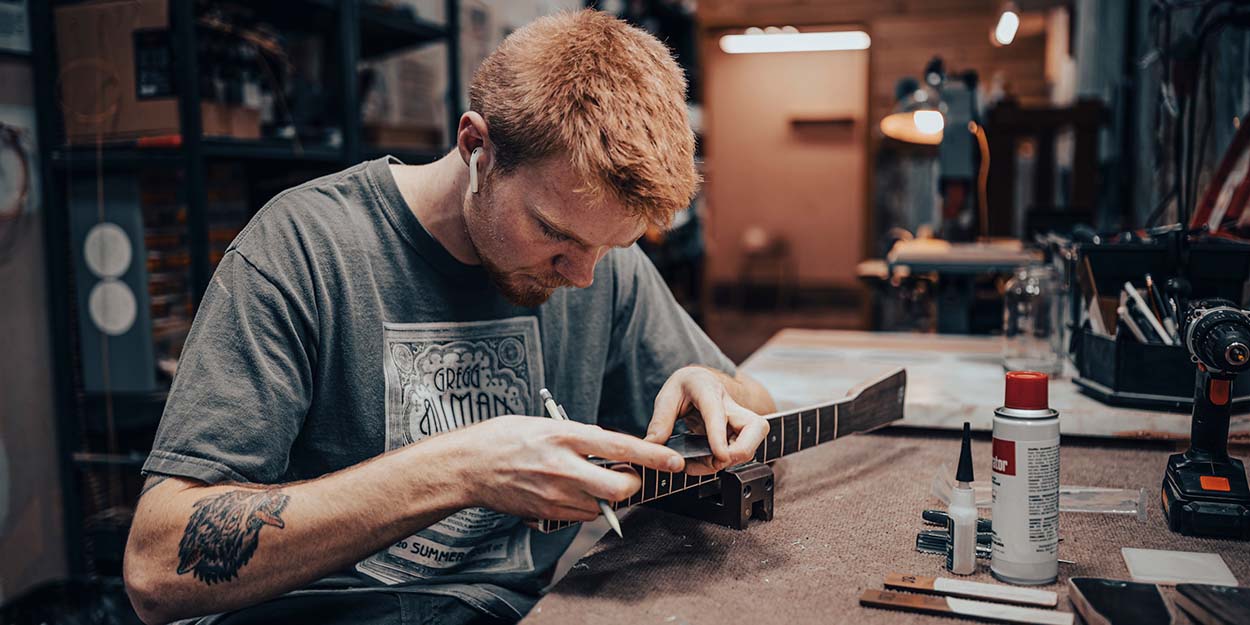 a worker is gluing the bridge of an acoustic guitar